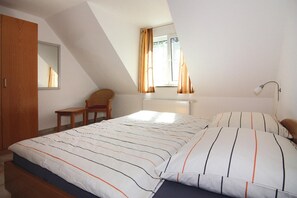 Et soveværelse med seng, stol, skrivebord, et vindue med gardiner og en radiator.