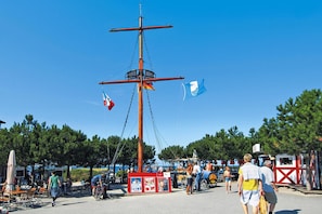 En kajebro med et højt mast, flag og folk der går.