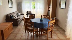 Un coin repas avec une table ronde, des chaises en bois, une nappe bleue et une bouteille de champagne.