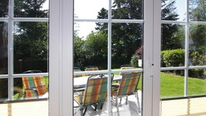 Un espace patio aménagé avec une table et des chaises, une porte-fenêtre coulissante et une vue sur un jardin.