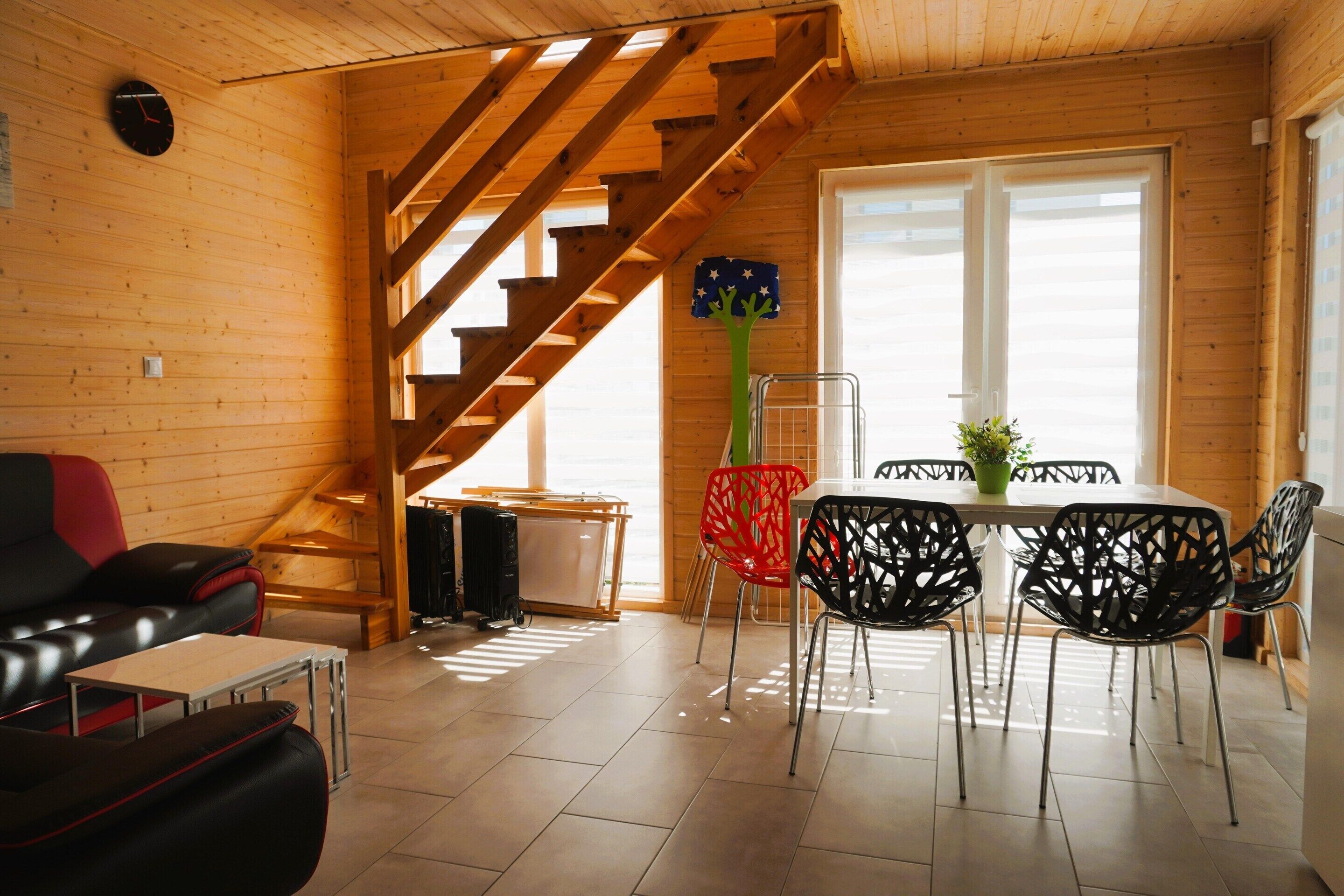 A wooden interior with a staircase, a dining area with chairs, a sofa, and a table.