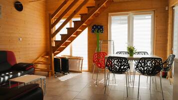 A wooden interior with a staircase, a dining area with chairs, a sofa, and a table.