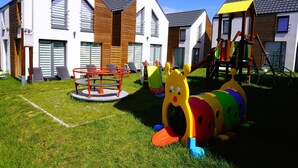 A playground with slides and climbing structures, surrounded by modern buildings with large windows and wooden accents. - Rewal Holiday Home Near Baltic Beach (Rewal)