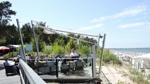 A glass-enclosed outdoor seating area with tables and chairs, overlooking a beach and a boardwalk. - Rewal Holiday Home Near Baltic Beach (Rewal)