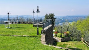 Eine begrünte Außengegend mit einer Steintreppe, die zu einer Aussichtsplattform führt, Metallstühlen und einem Geländer mit Blick auf eine entfernte Landschaft.