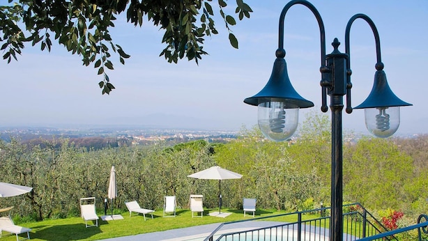 Ein Poolbereich mit Blick auf eine Stadtlandschaft, Liegestühle und eine glockenförmige Leuchte.