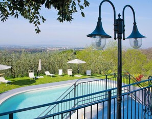Un espace aménagé au bord de la piscine, offrant une vue sur le paysage urbain, avec des chaises longues et un luminaire en forme de cloche.