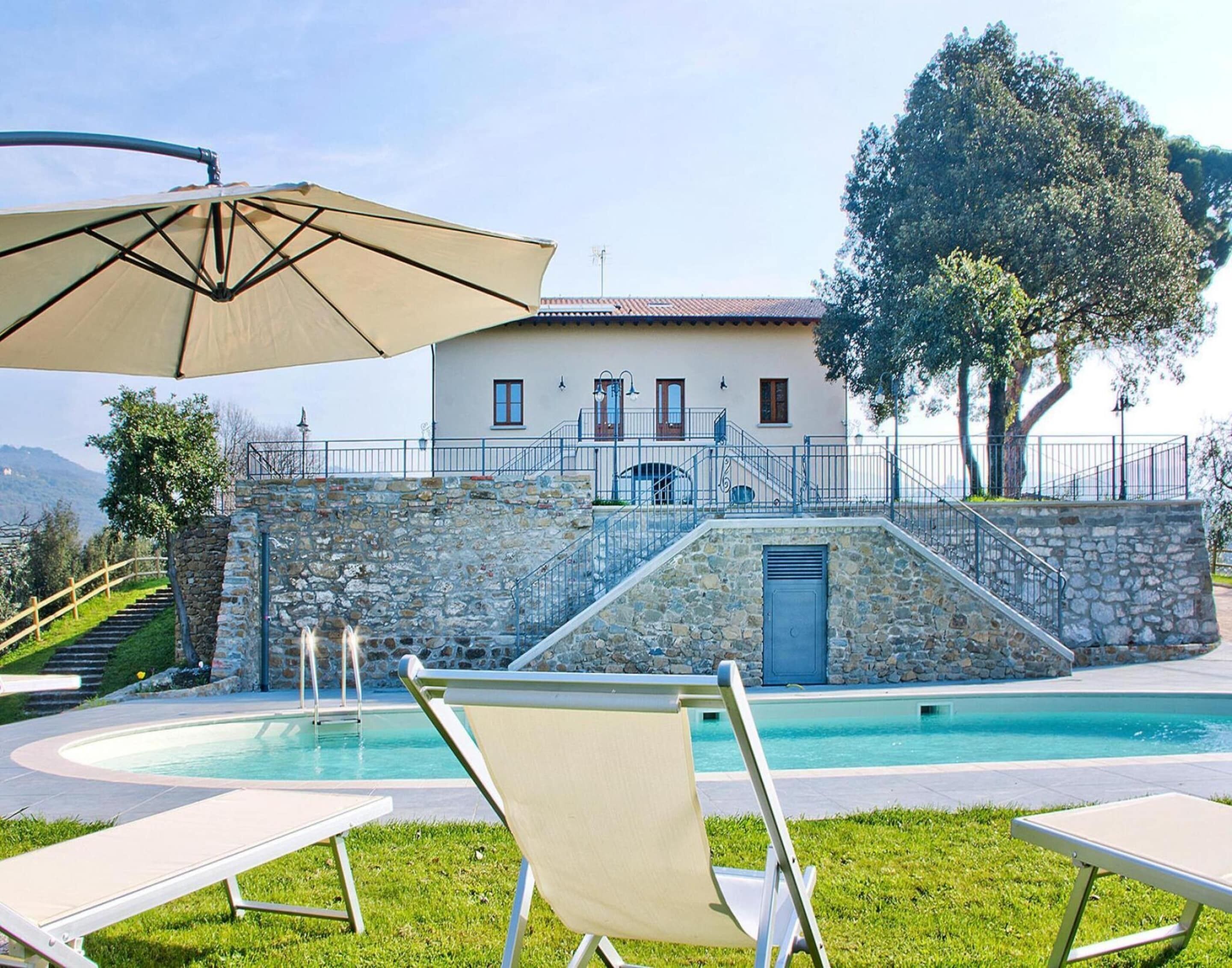 A pool area with lounge chairs, a stone wall, and a building with a tiled roof.