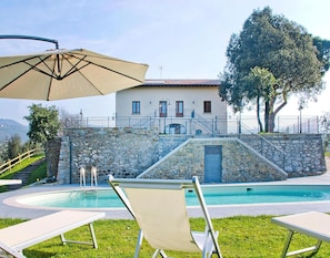 Un espace piscine avec des chaises longues, un mur en pierre et un bâtiment doté d’un toit en tuiles.