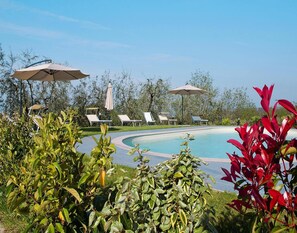 Area piscina con lettini e ombrelloni, immersa nel verde.