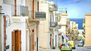 Una stretta via fiancheggiata da edifici, balconi e auto parcheggiate.