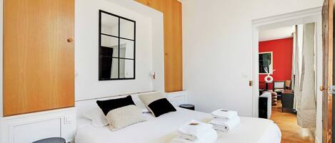 A modern hotel room with a large bed, wooden paneling, a mirror, and a red accent wall.