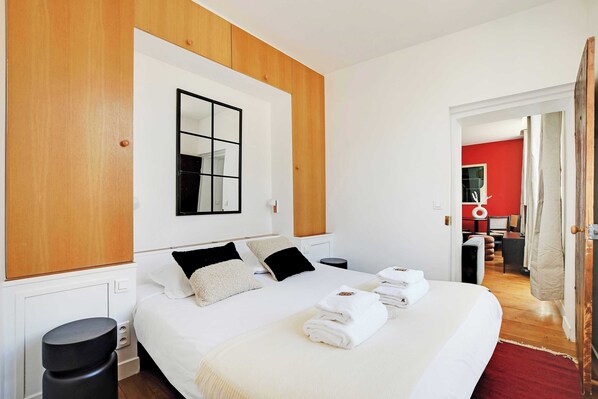 A modern hotel room with a large bed, wooden paneling, a mirror, and a red accent wall. - Résidence Paris BRETONNERIE (Paris)