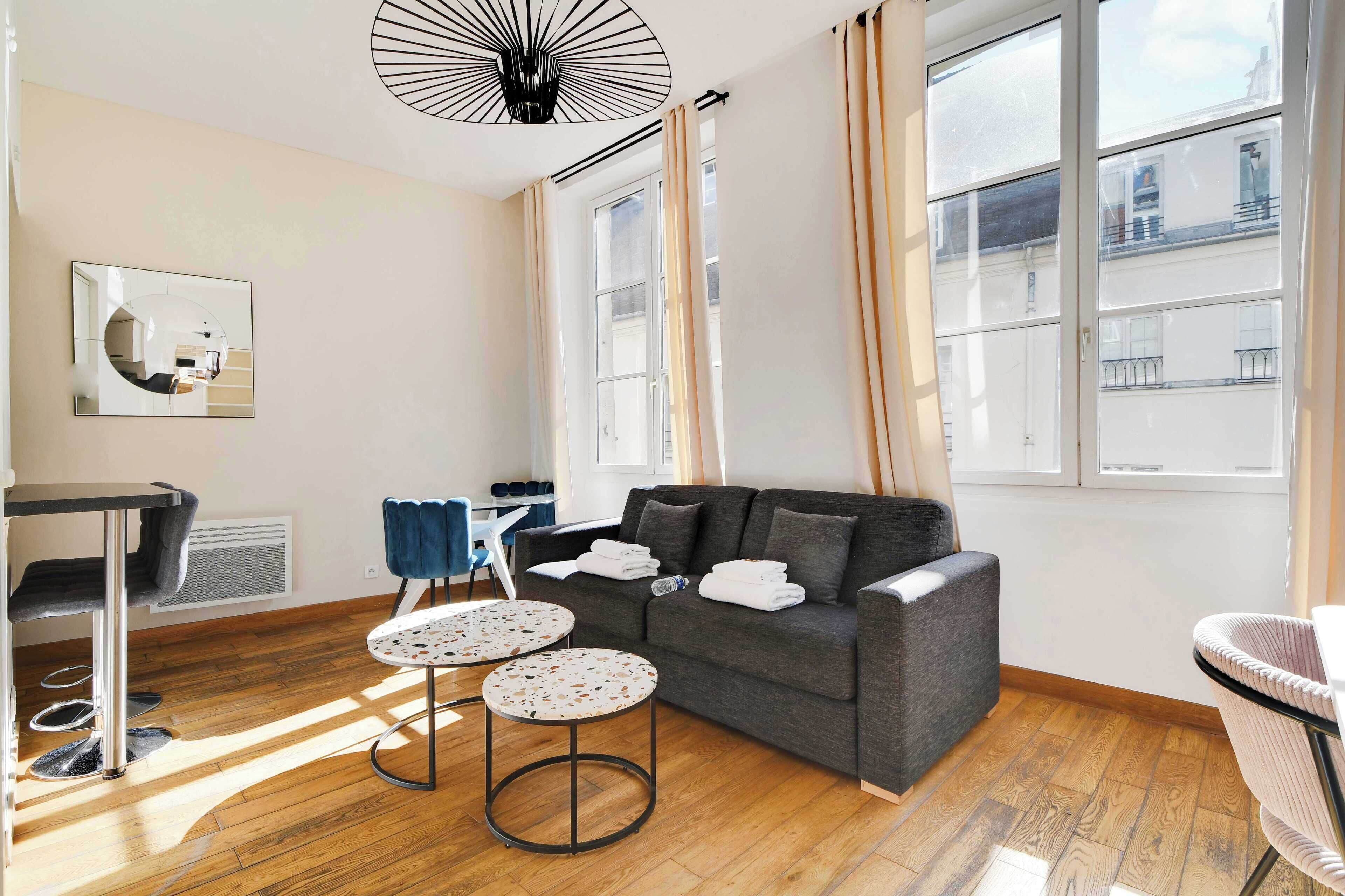 A modern living room with a grey sofa, two round tables, and a large window with curtains.