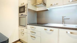 A modern kitchen with white cabinets, a built-in oven, a microwave, and a stainless steel sink. - Résidence Paris BRETONNERIE (Paris)