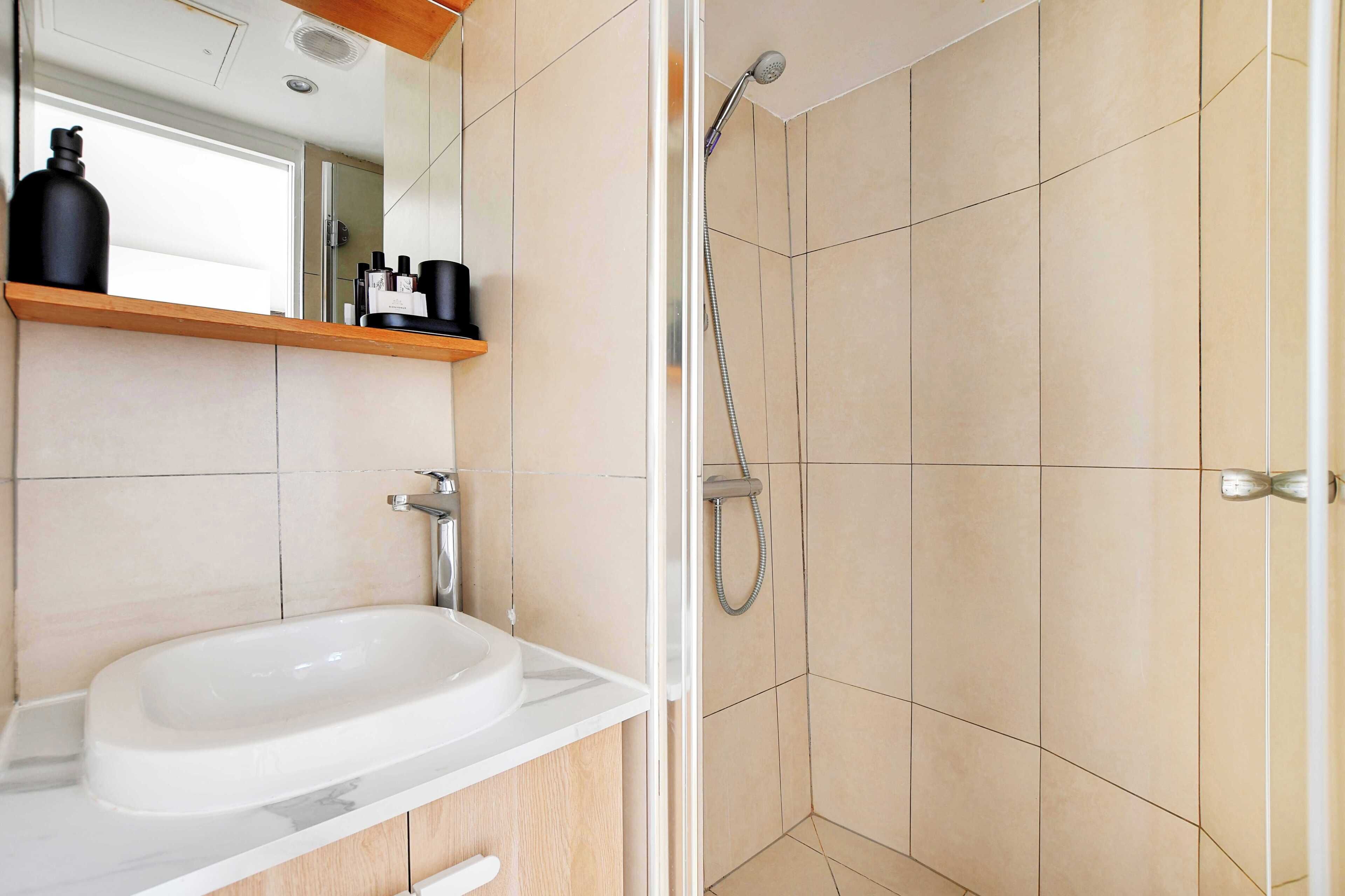 Une salle de bain moderne avec un lavabo blanc, un miroir et une douche aux carreaux de couleur beige.