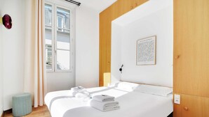 A hotel room with a large bed, a wooden wardrobe, a framed artwork on the wall, and a window with curtains. - Résidence Paris BRETONNERIE (Paris)
