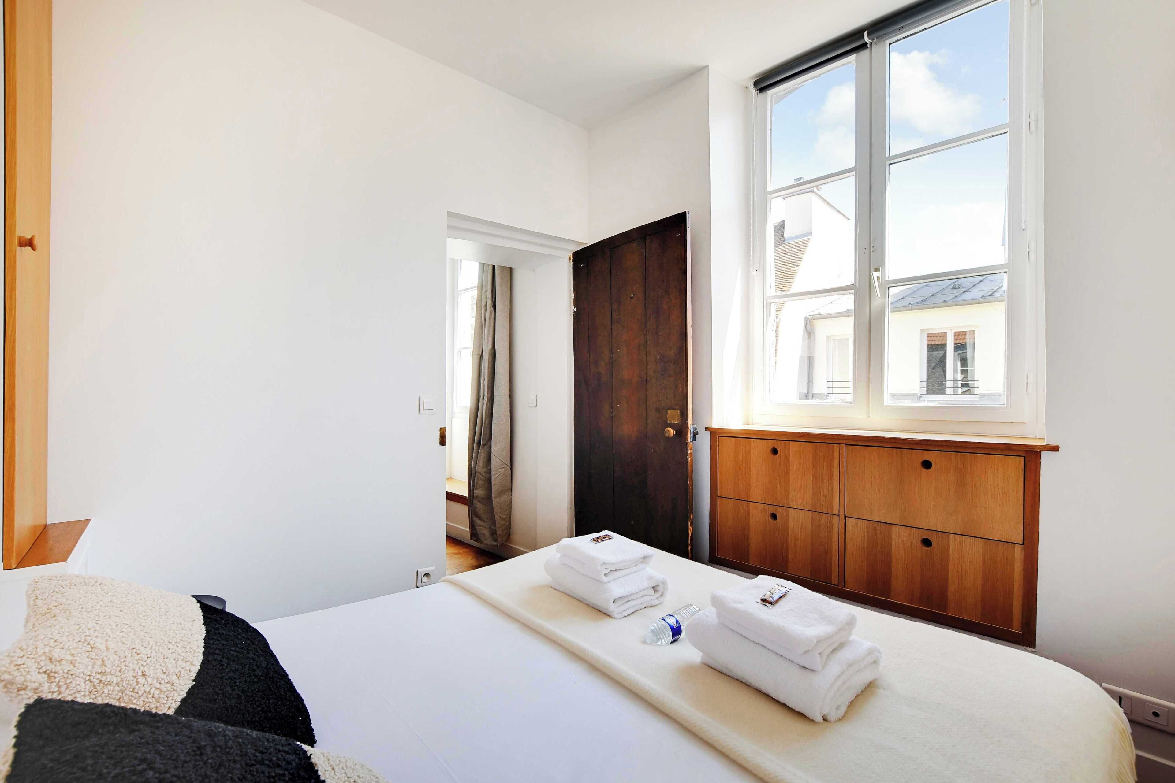 A hotel room with a bed, a wooden wardrobe, a window with a view, and a door leading to another room.