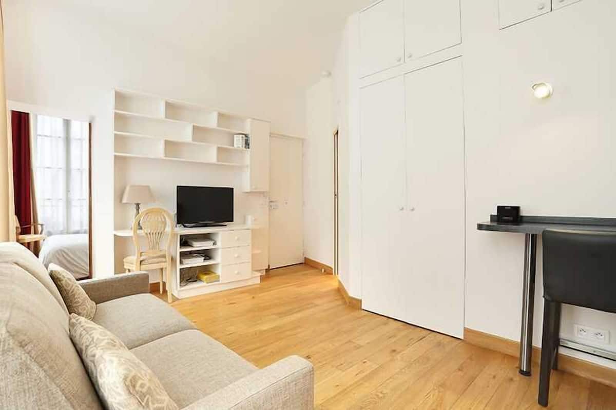 A modern living room with a sofa, TV, white shelving, and a dining area.