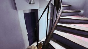 A staircase with a handrail, a blue door, and a light fixture on the wall. - Résidence Paris BRETONNERIE (Paris)