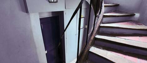 A staircase with a handrail, a blue door, and a light fixture on the wall.