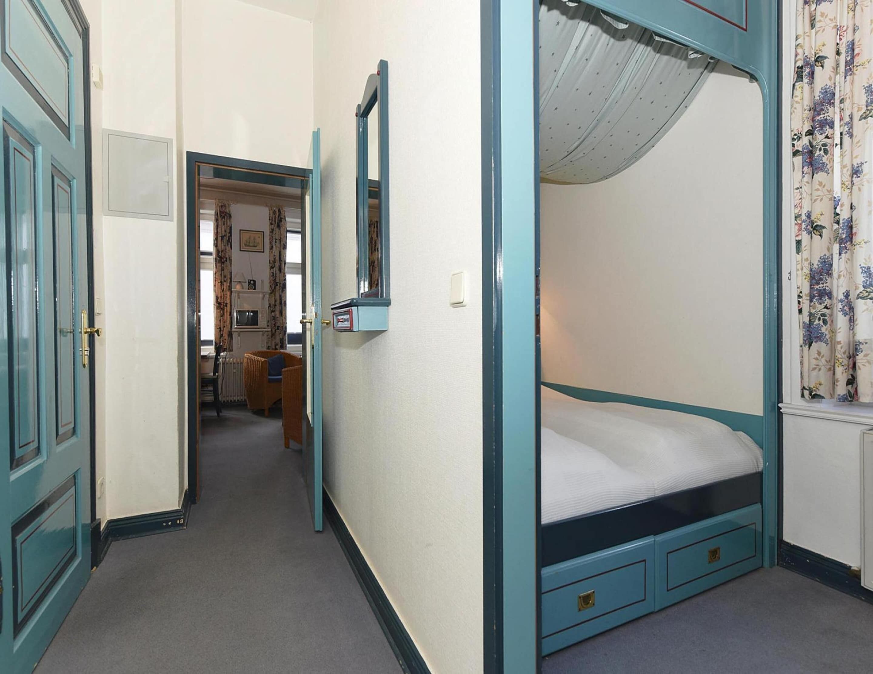 A narrow hallway leading to a bedroom with a single bed, a small chair, and a mirror on the wall.