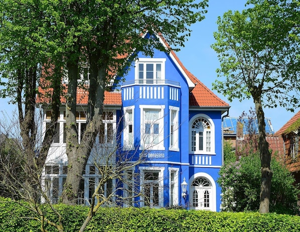 A blue building with a red roof, surrounded by trees and greenery.