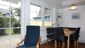 A dining area with a table and chairs, a window with blinds, and a pendant light. - Ferienwohnung in Trassenheide (Trassenheide)