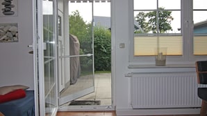 A room with a sliding glass door leading to a patio, a radiator, and a window with blinds. - Ferienwohnung in Trassenheide (Trassenheide)