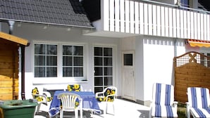 A patio with a table and chairs, a wooden fence, and a white building with windows. - Ferienwohnung in Trassenheide (Trassenheide)