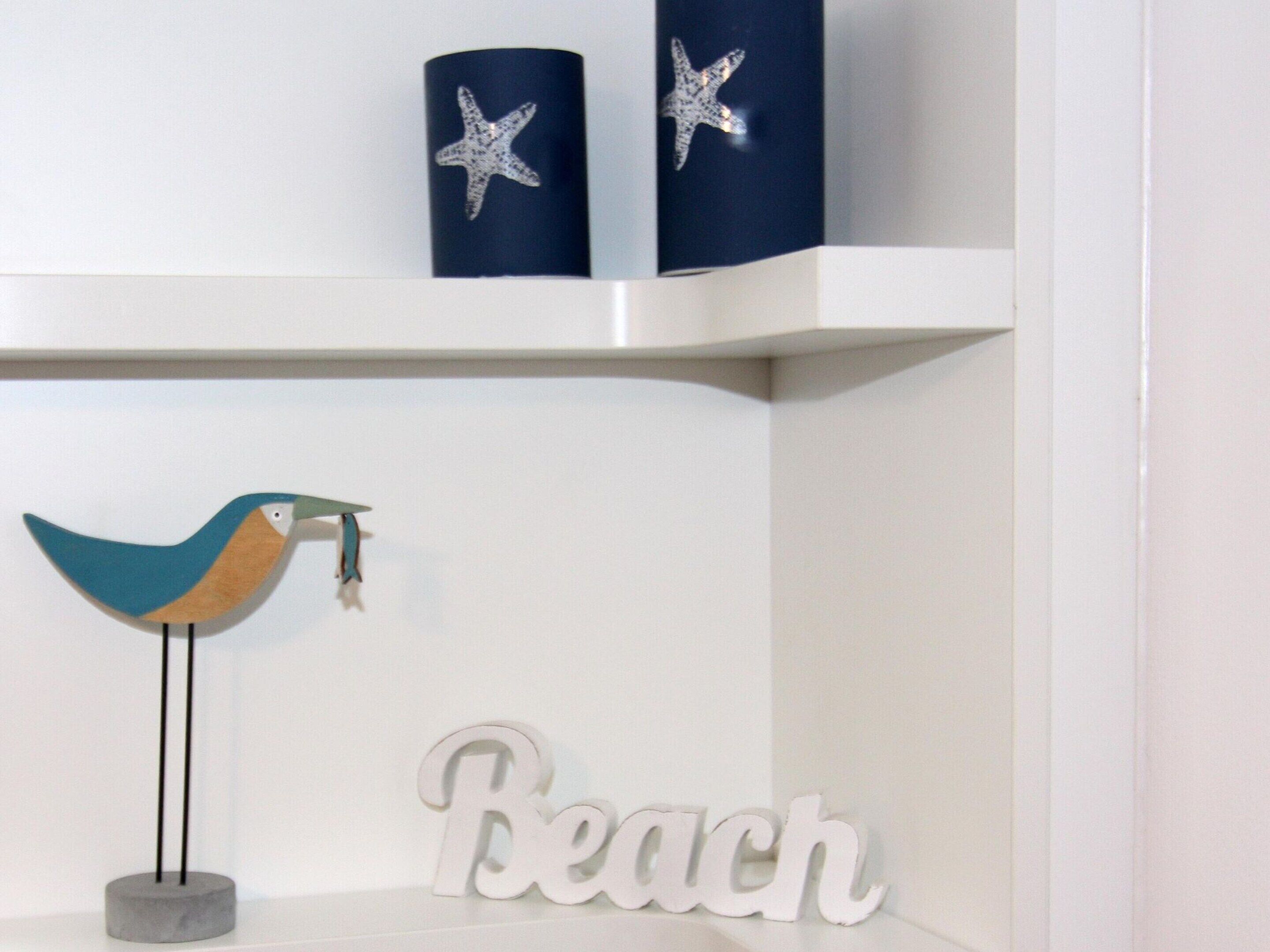 Une étagère ornée d’objets décoratifs, notamment un oiseau, une étoile de mer et une pancarte indiquant « Plage ».