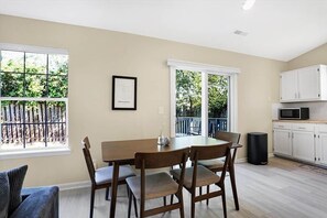 A dining area with a table and chairs, a framed picture on the wall, and a view through the window.