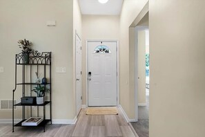 Un couloir avec une porte blanche, une étagère en métal noir ornée de plantes et un mur de couleur beige.