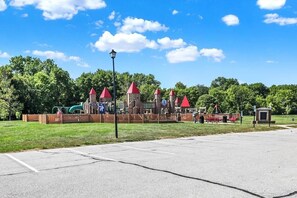 Une aire de jeux avec des structures colorées aux toits rouges, un toboggan vert et un petit bâtiment.