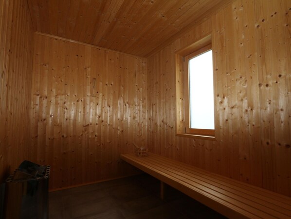 A wooden cabin interior with a bench, a window, and a trash bin.