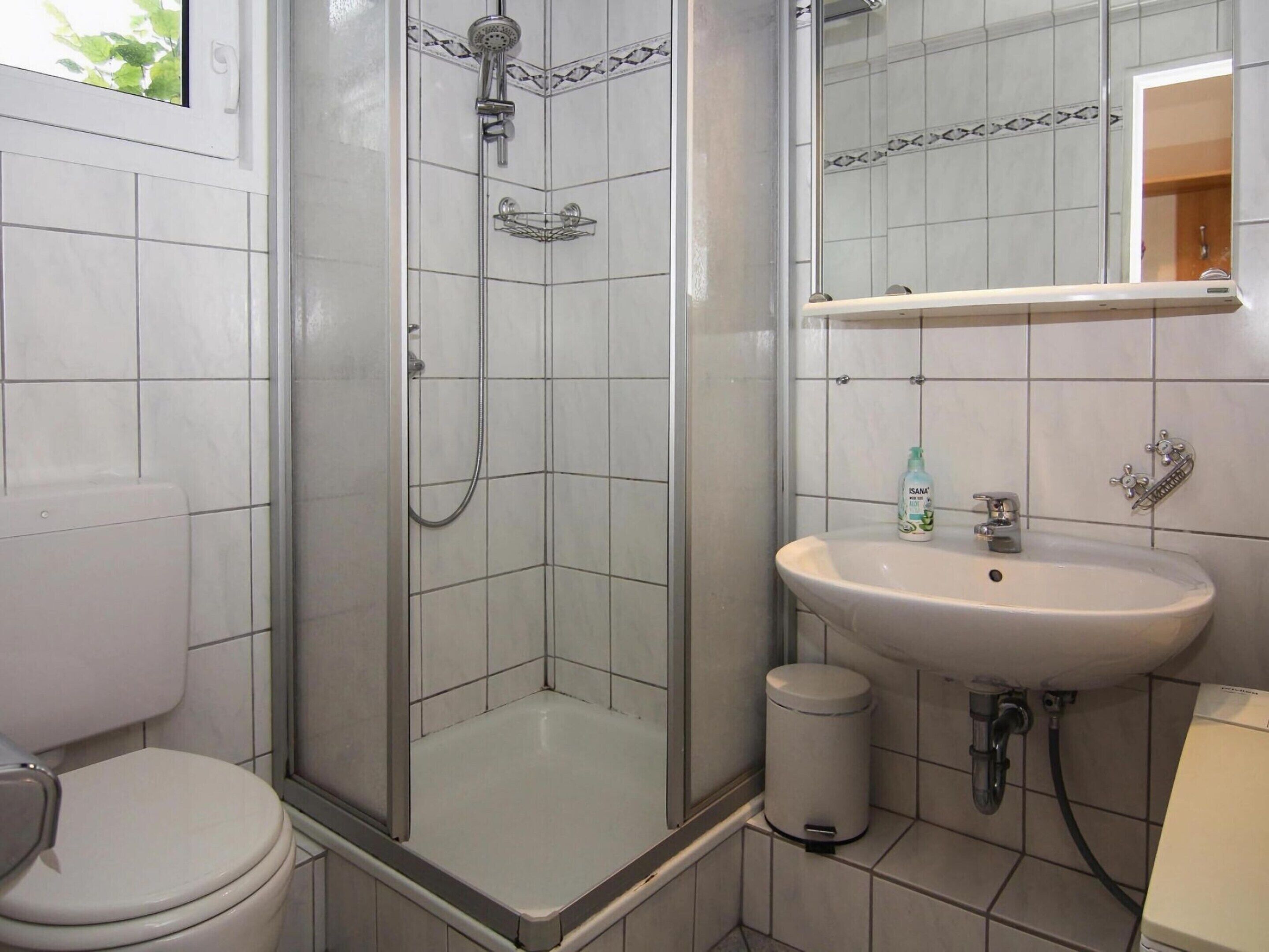 Ein Badezimmer mit Dusche, Toilette, Waschbecken und einem Mülleimer.