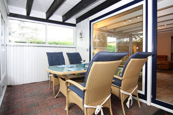 A covered patio with wicker furniture and a glass table, overlooking a garden. - Attraktiver Bungalow in Warwerort an der Nordsee (Warwerort)