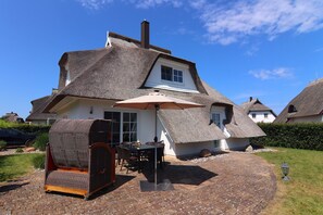 A traditional thatched-roof house with a patio area, a dining table, and a covered seating area. - Ferienhaus Weisse Dune, Zinnowitz (Zinnowitz)