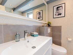 A modern bathroom with a large white sink, chrome faucet, and a toilet. There are two framed pictures on the wall, a small plant on the sink, and a towel rack. - Apartement in Top Lage (St. Peter-Ording)