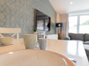 A dining area with a table set with bowls and cups, a glass pitcher, and a modern kitchen in the background. - Apartement in Top Lage (St. Peter-Ording)