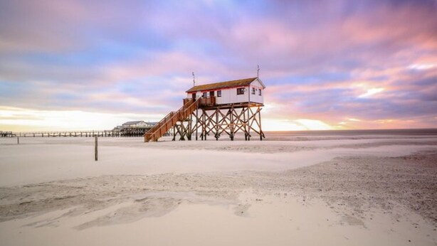 A beach house with a wooden deck and stairs leading to a small building.