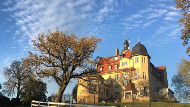 A large, historic building with a prominent dome and red-tiled roof, surrounded by a white fence and trees. - Chalet in Wendorf (Kuhlen-Wendorf)