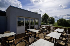 An outdoor patio area with tables and chairs, a building with large windows, and a view of the countryside. - Ferienpark Harz in Hasselfelde (Oberharz am Brocken)
