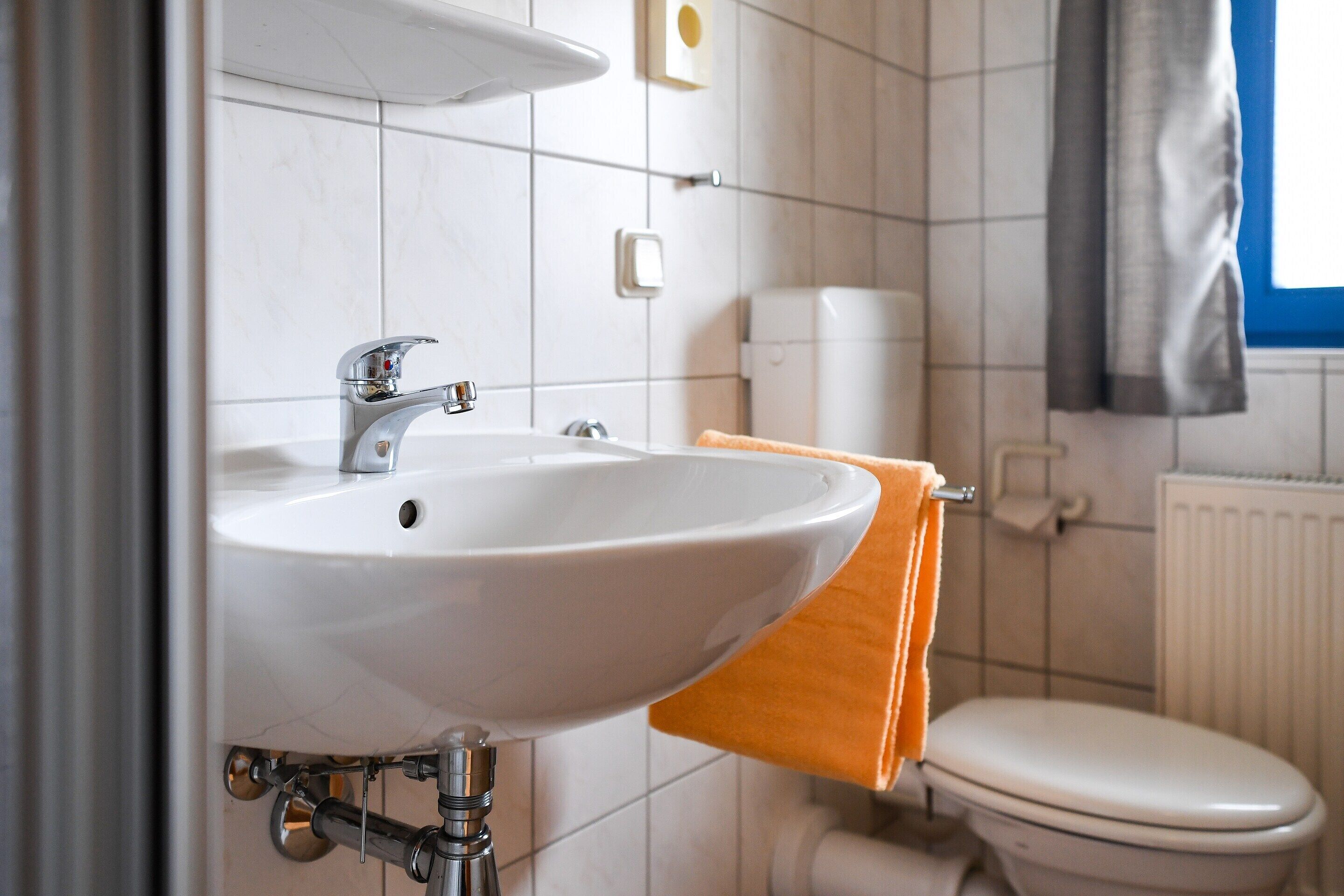A bathroom with a white sink, a toilet, and a towel rack with an orange towel.
