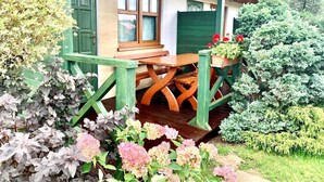 A wooden table and bench under a covered porch with green railings, surrounded by various plants and flowers. - Comfortable Holiday Homes, Close to the Beach (Mielno)