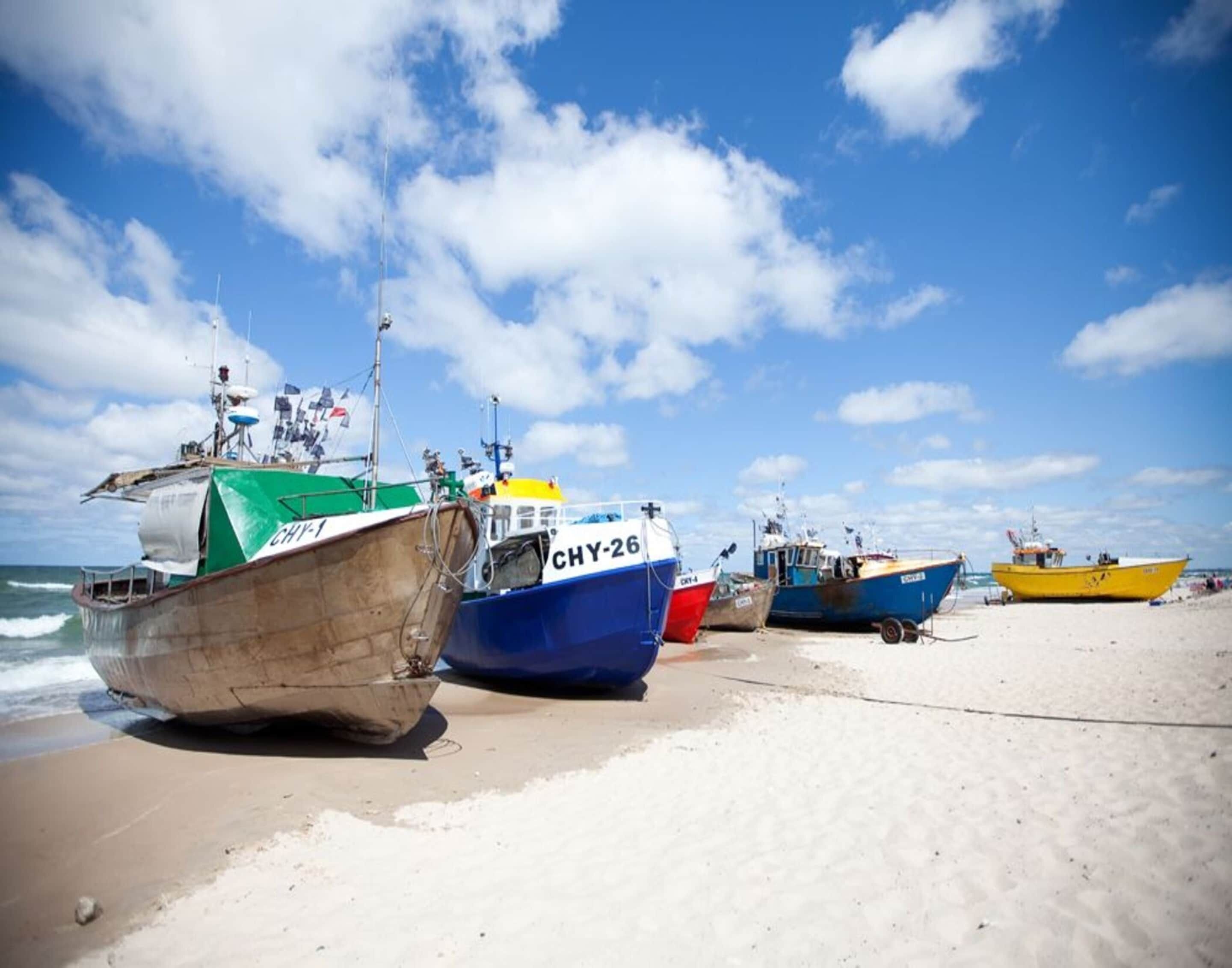 Several boats moored on a sandy beach with the ocean in the background.