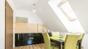 A modern kitchen with black cabinets, a wooden floor, and a skylight above a dining area with a table and chairs. - Apartment in Krynica Morska Near Vistula Lagoon (Krynica Morska)