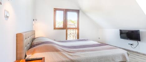 A bedroom with a bed, a bedside table, a television mounted on the wall, and a window with a view of the outside.