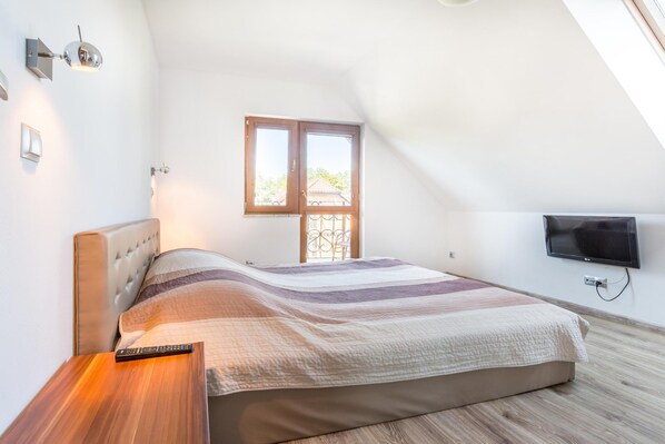 A bedroom with a bed, a bedside table, a television mounted on the wall, and a window with a view of the outside.