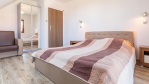 A bedroom with a large bed, a wooden wardrobe, a mirror, and a brown armchair. - Apartment in Krynica Morska Near Vistula Lagoon (Krynica Morska)